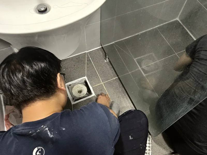 윗집 욕실 배수구·줄눈 누수 보수 중 배수구 둘레를 정리하는 작업자