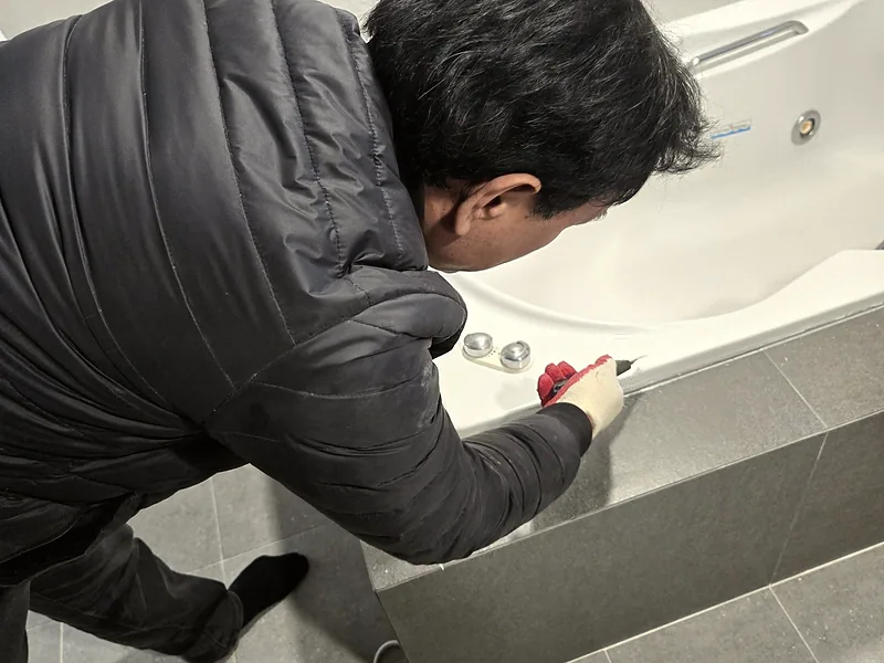 월풀 욕조 모터 교체 중 욕조 앞판 점검구를 여는 기술자