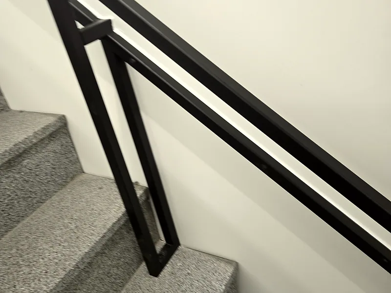 계단 손잡이 설치 후 가벽을 따라 고정된 블랙 철제 손잡이