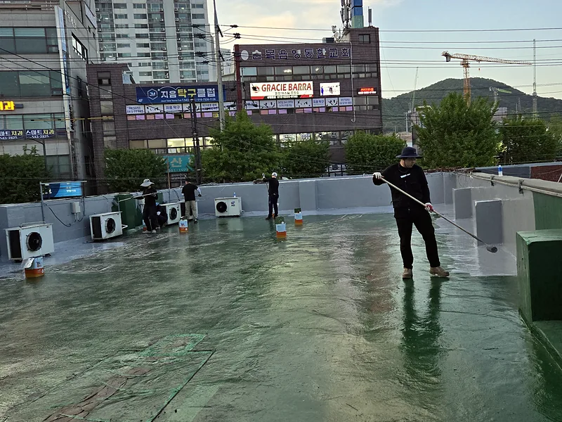 옥상 누수 보수 현장 롤러로 방수제를 바르는 작업자
